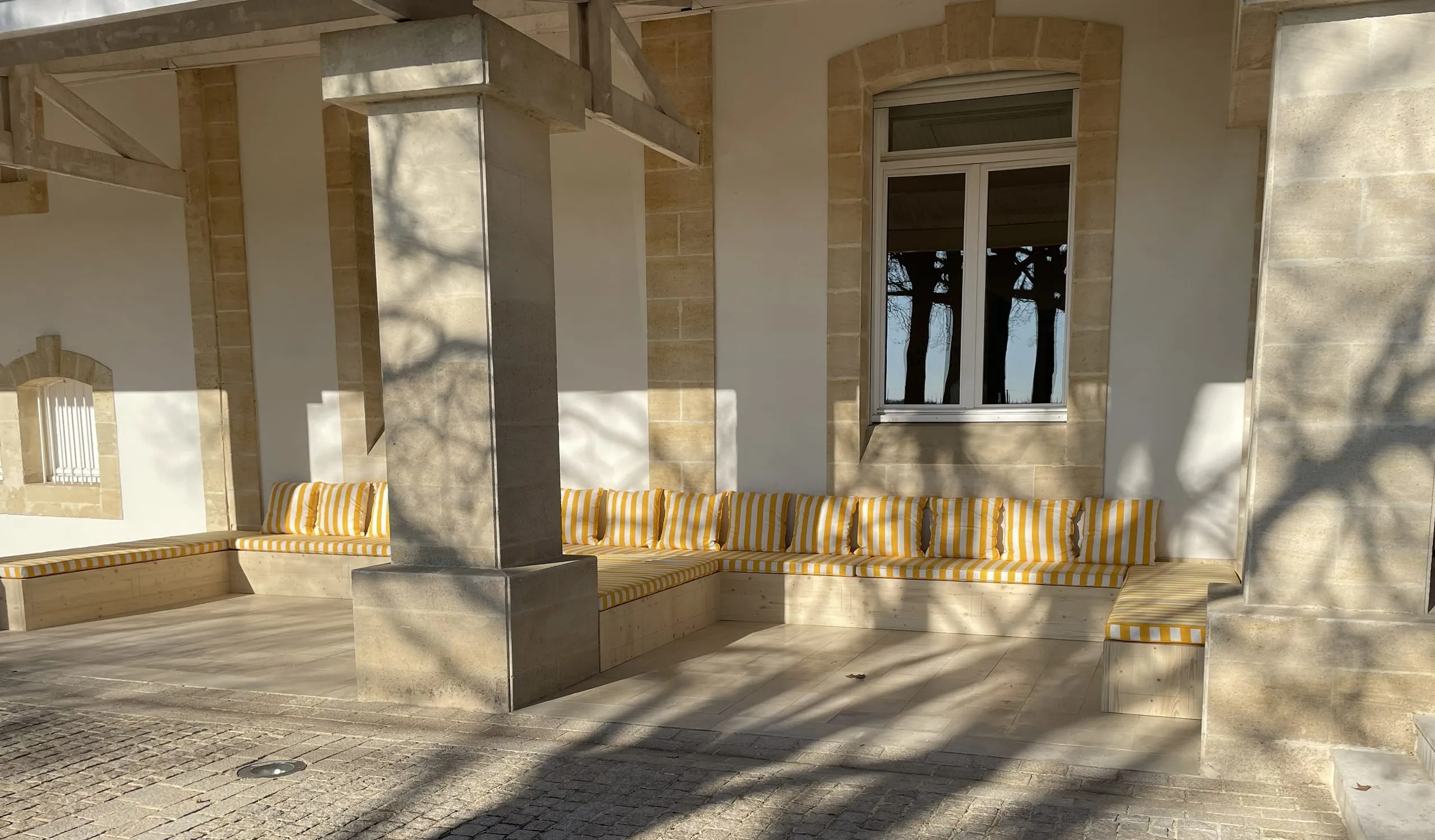 Longues banquettes en bois avec coussins rayés sous une terrasse couverte