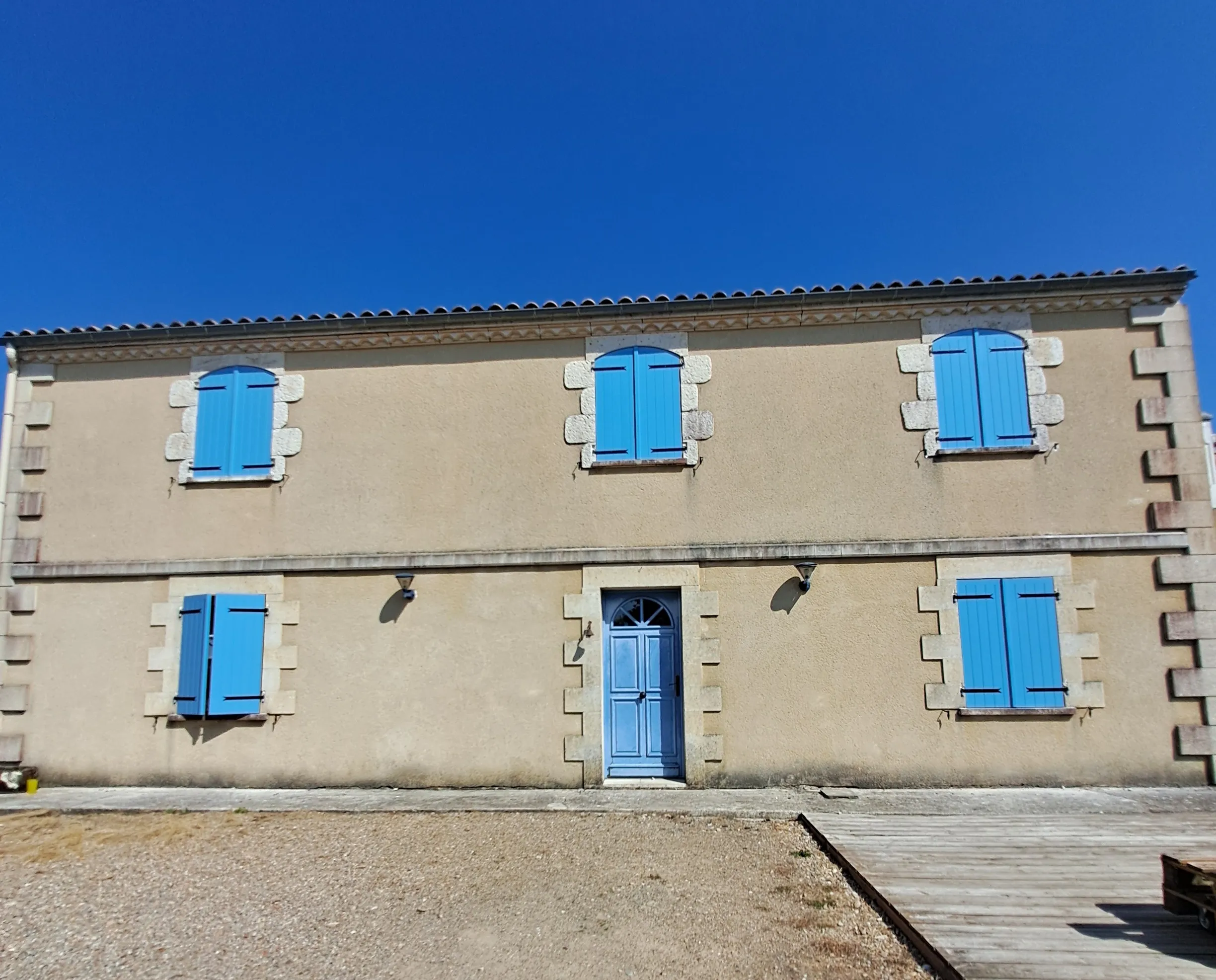 Façade claire avec porte et volets battants peints en bleu