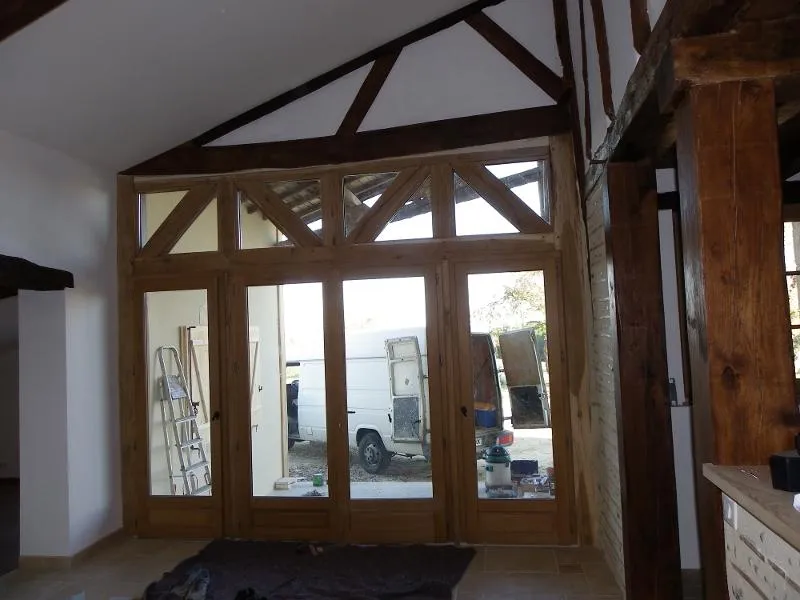Portes françaises vitrées en bois vues depuis l’intérieur sous des poutres anciennes