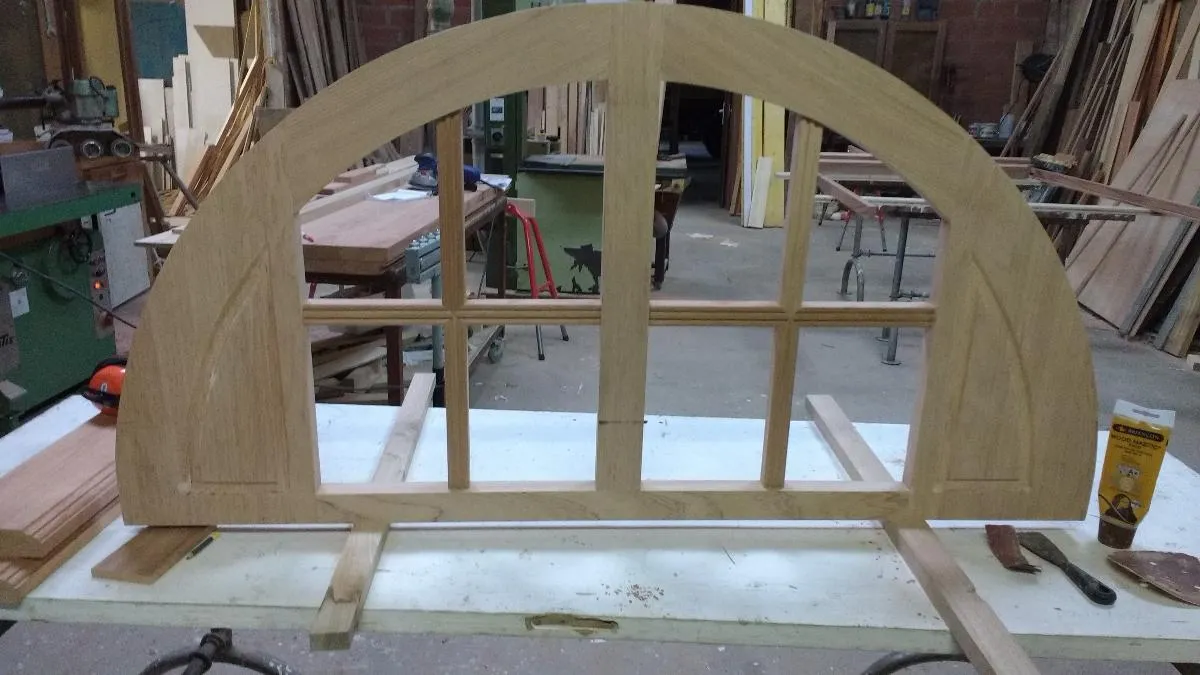 Imposte vitrée cintrée en bois posée sur un établi dans l’atelier