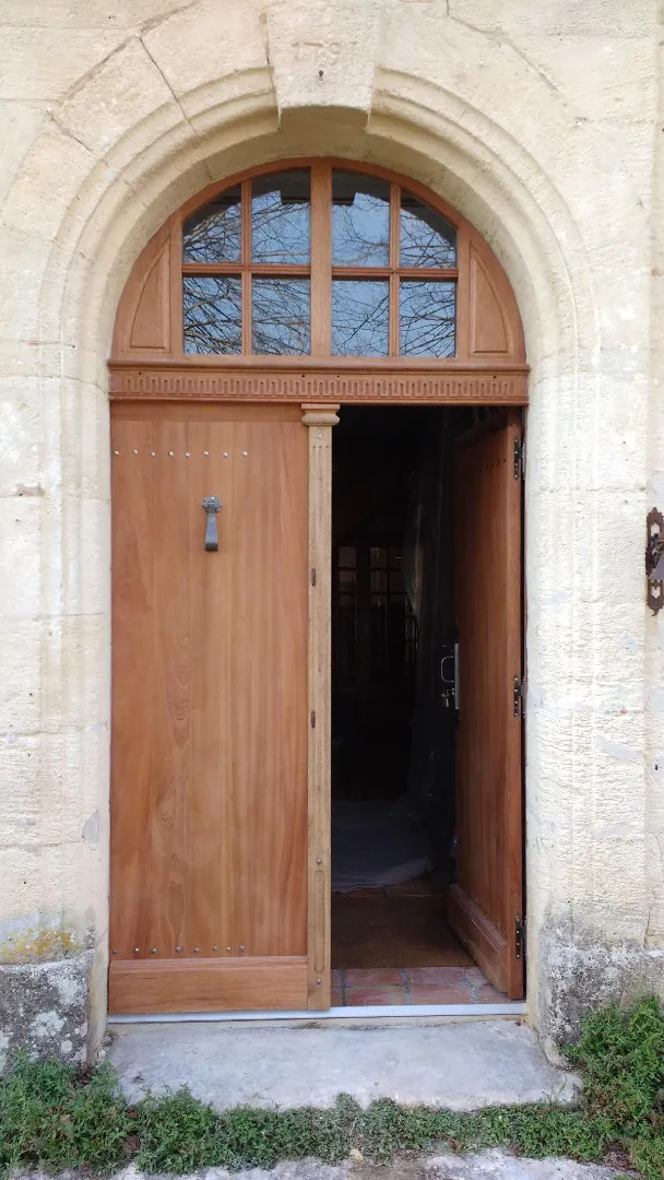 Porte d’entrée cintrée en bois entrouverte sous une imposte vitrée
