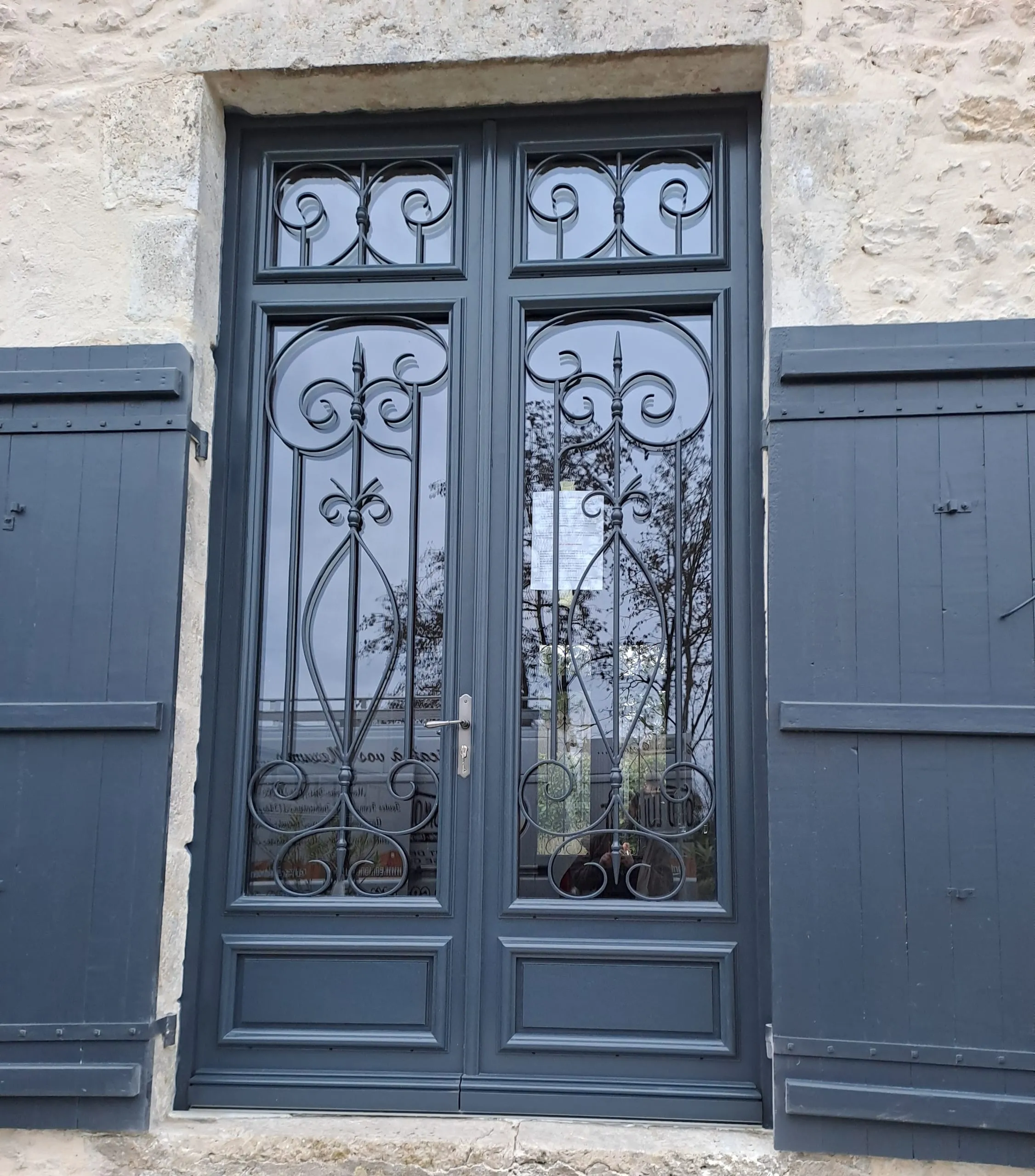Porte d'entrée vitrée à deux vantaux avec ferronnerie décorative sur une façade en pierre