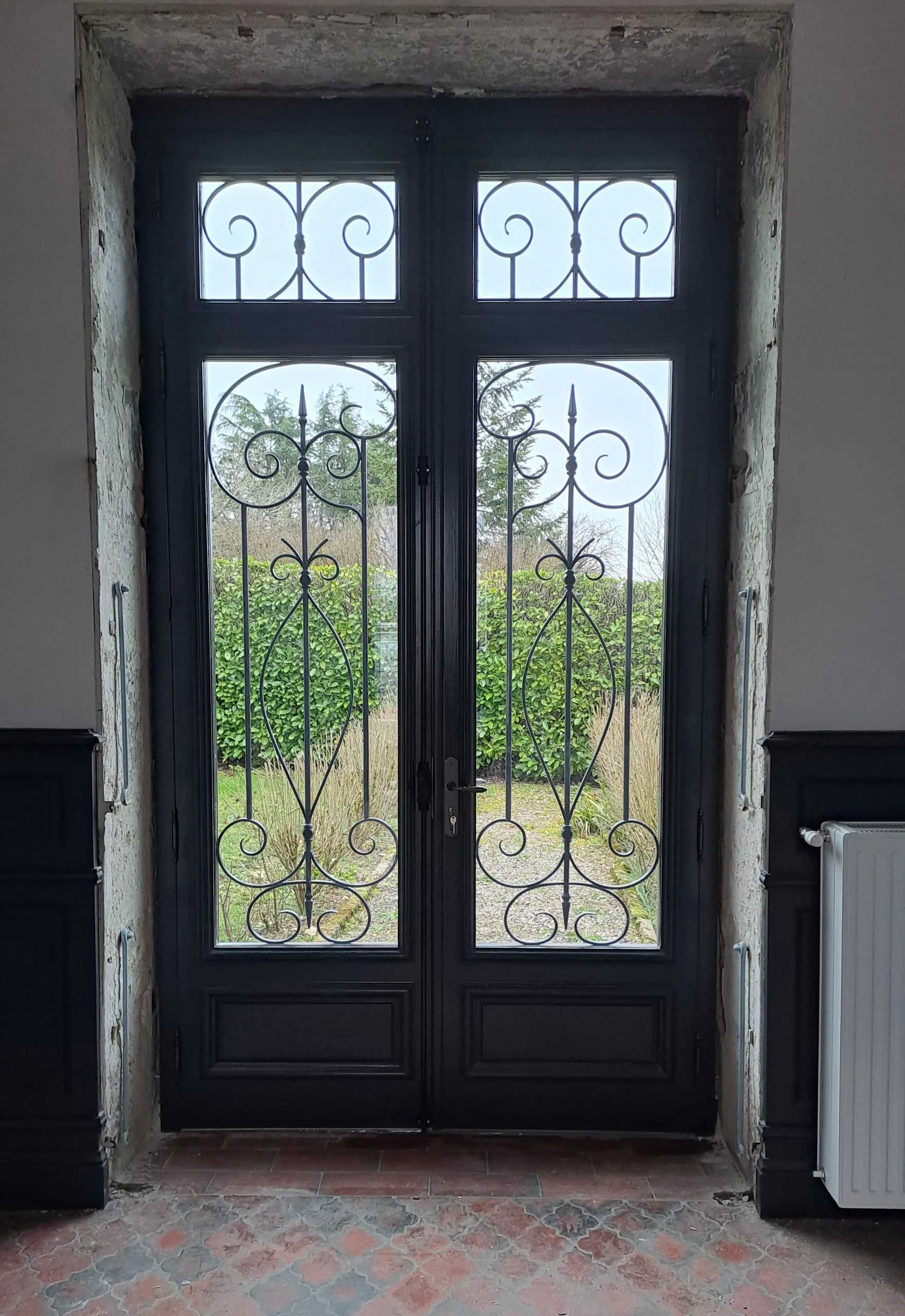 Porte d'entrée sombre à deux vantaux avec ferronnerie décorative vue depuis un intérieur